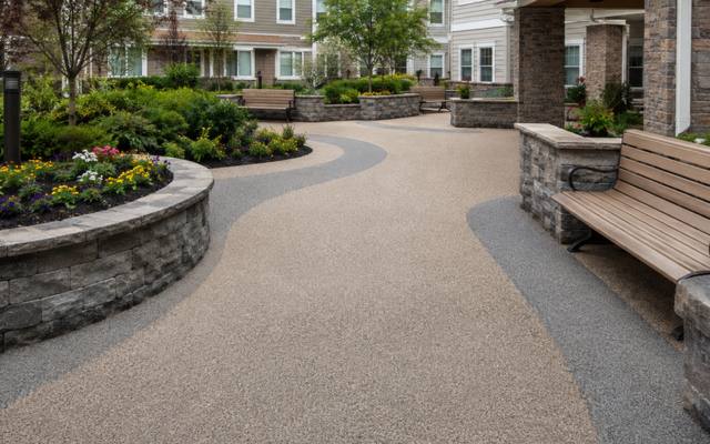 Curved tan rubber walkway through a courtyard with stone planters and a bench